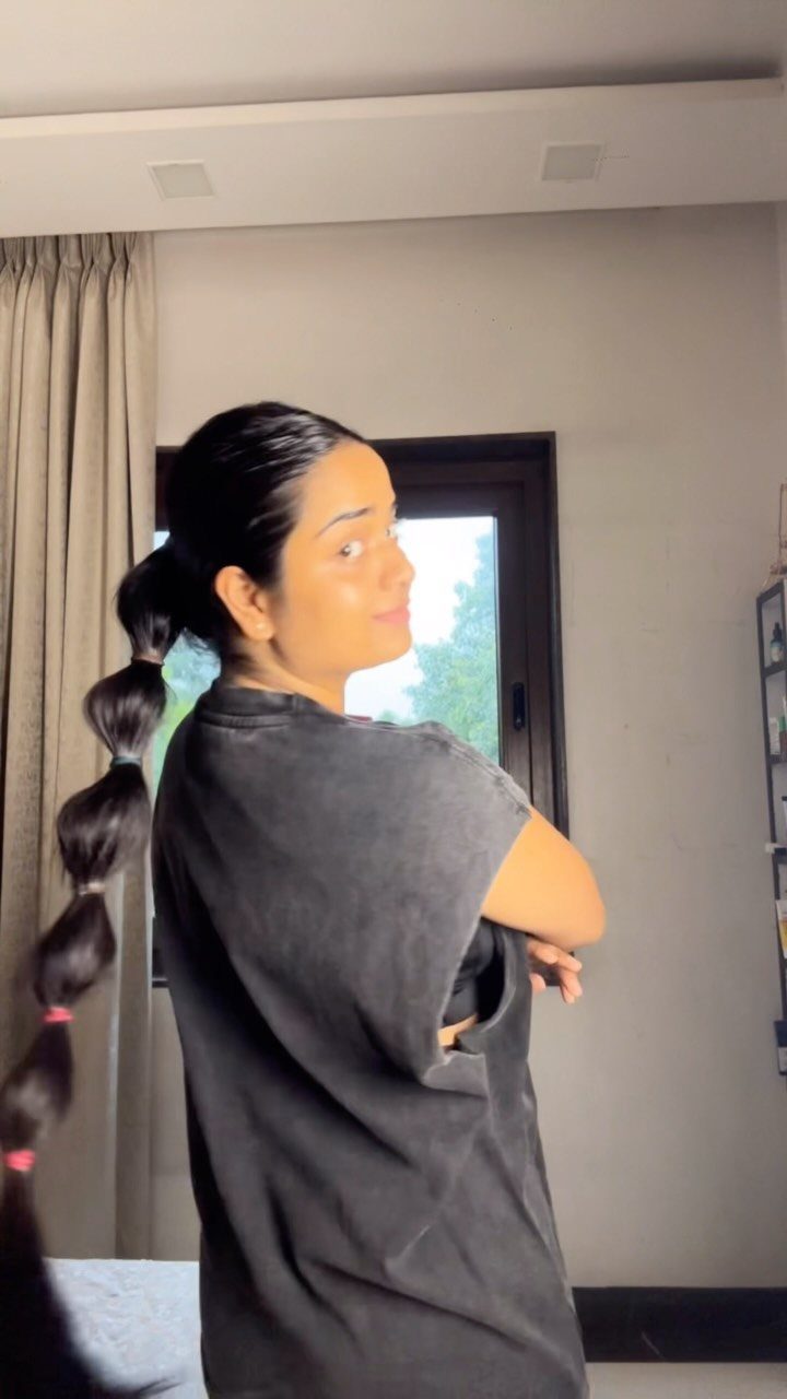 Woman with a long bubble ponytail wearing a grey t-shirt posing indoors.