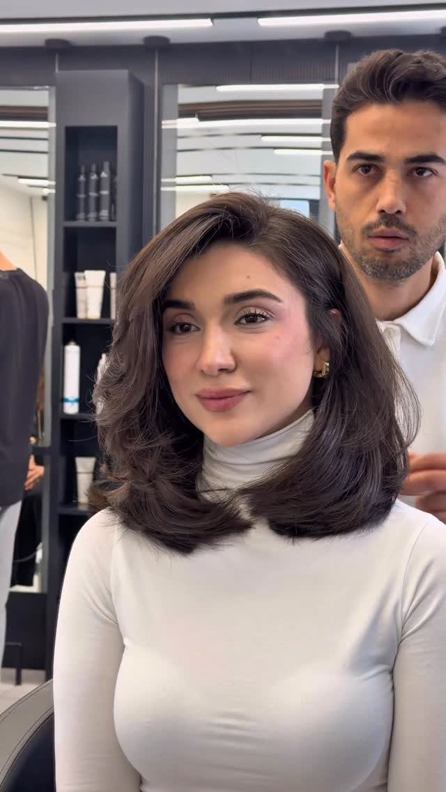Woman with a brown curved lob hairstyle wearing a white turtleneck in a salon