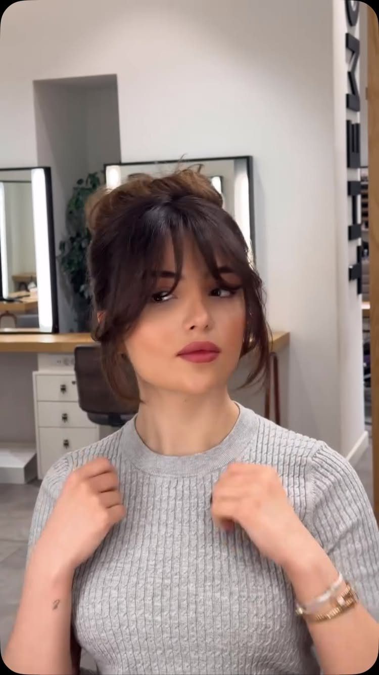 Woman with brown hair in a loose updo and bangs wearing grey sweater