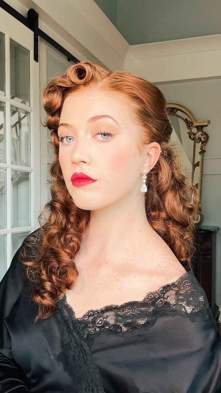 Woman with red hair styled in glamorous Old-Hollywood waves and red lipstick.