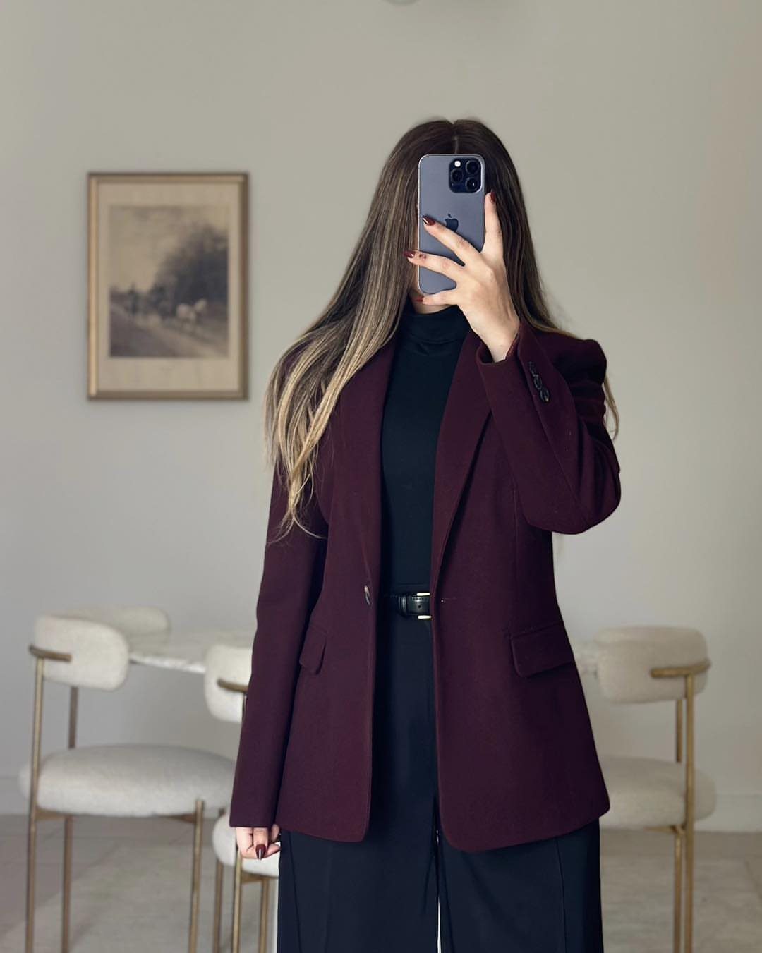 Woman wearing a burgundy blazer and black trousers taking a mirror selfie indoors.