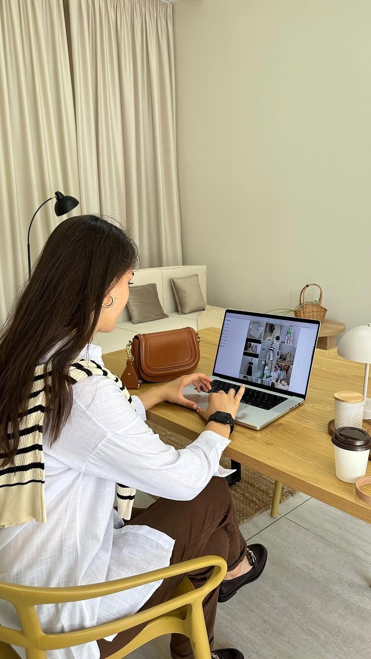 Woman in white shirt and brown trousers working on a laptop at a table