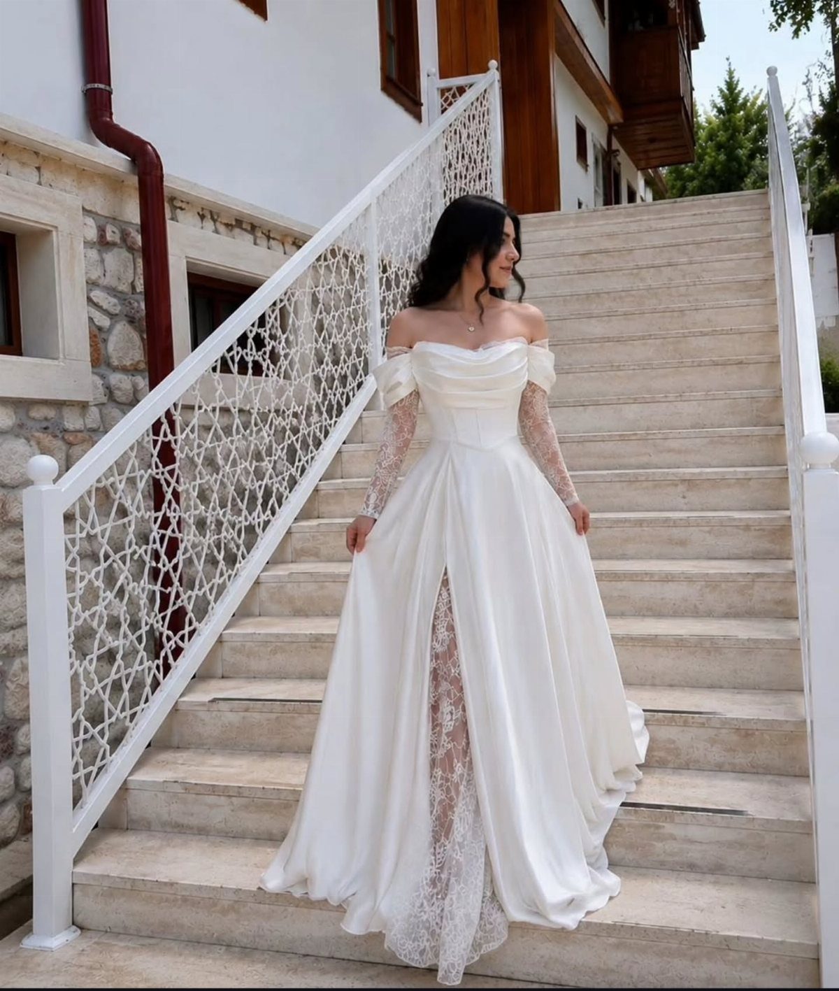 Woman in a white off-the-shoulder wedding dress with lace sleeves on white stairs