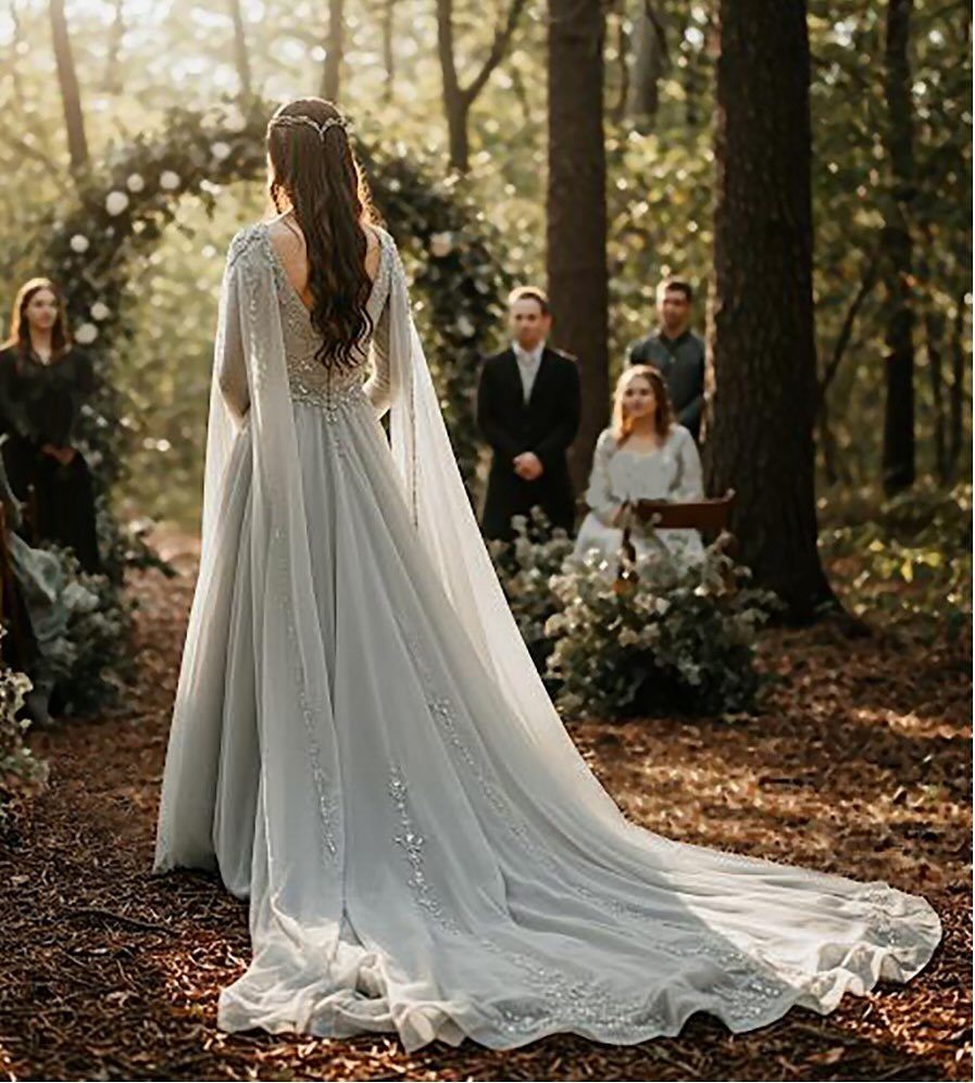 Woman in a light blue-grey flowing wedding gown standing in a forest setting.