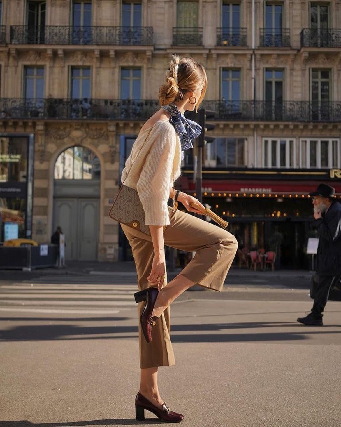 Woman in tan trousers wearing burgundy block-heel loafers on a city street.