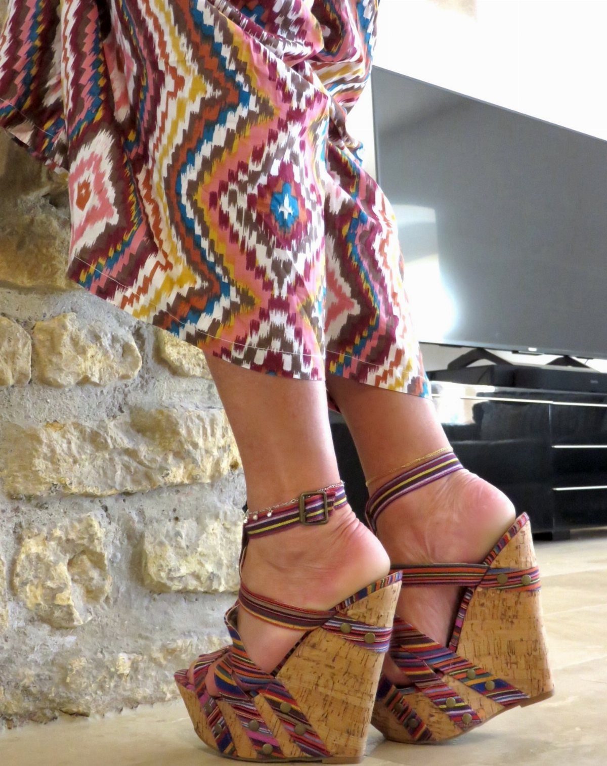 Colorful patterned wedge sandals with cork heels worn with matching patterned trousers.