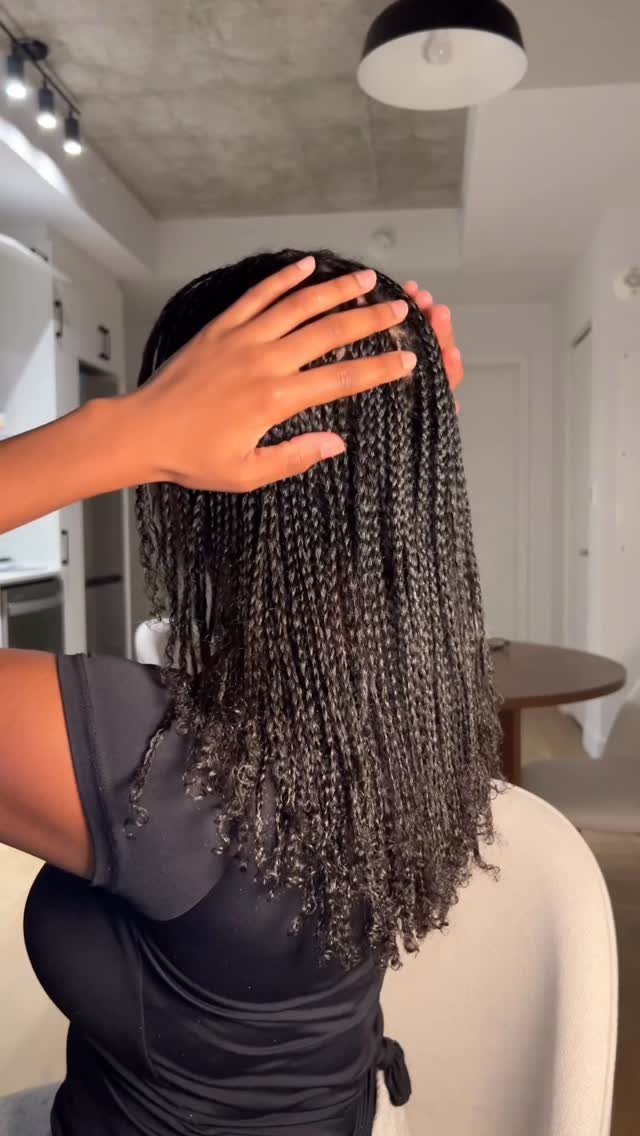 Woman with long dark micro-braids touching her hair in a bright room