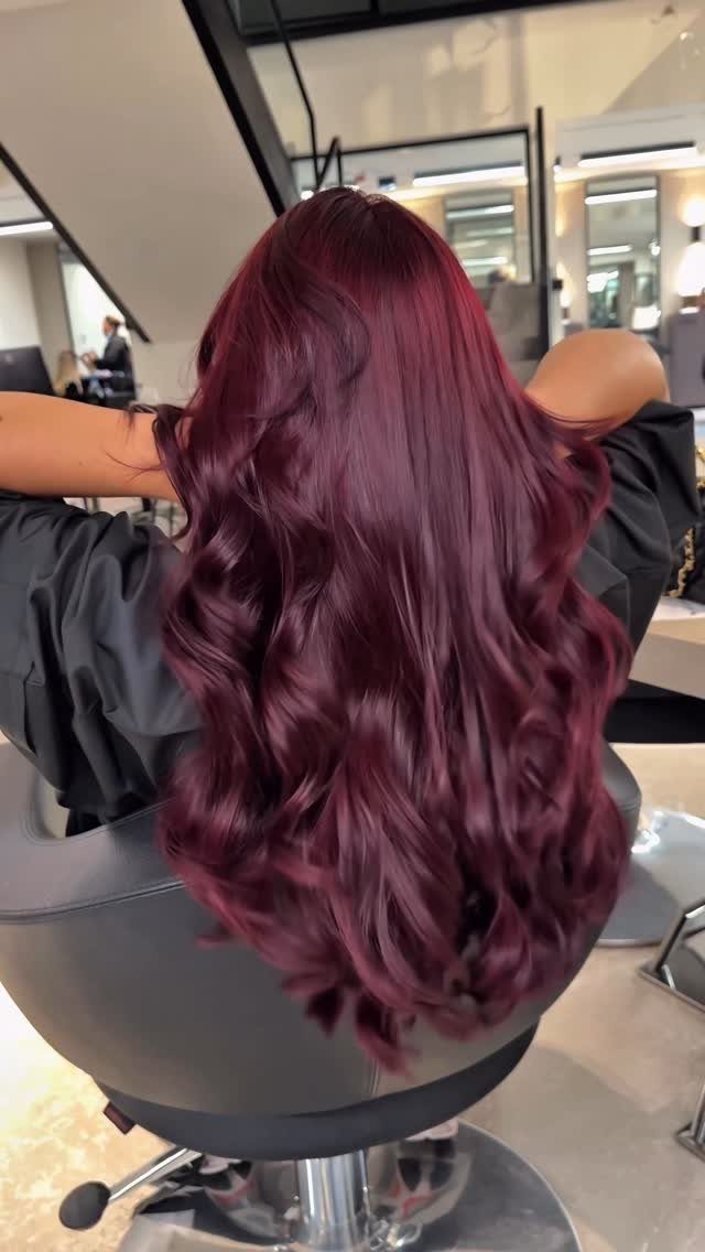 Long wavy maroon hair shown from the back in a professional salon setting.