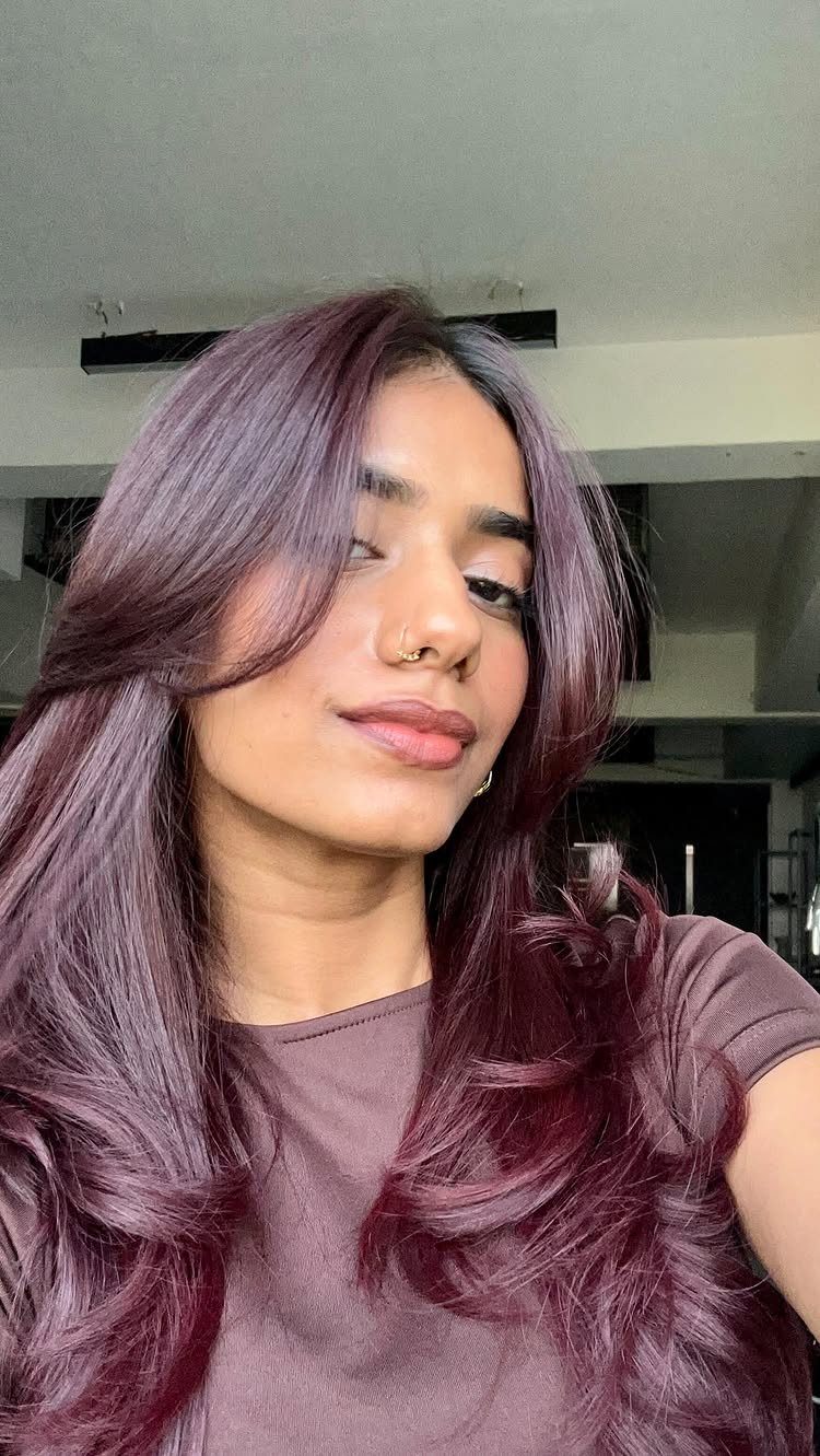 Woman with long wavy maroon hair wearing a matching brown t-shirt.