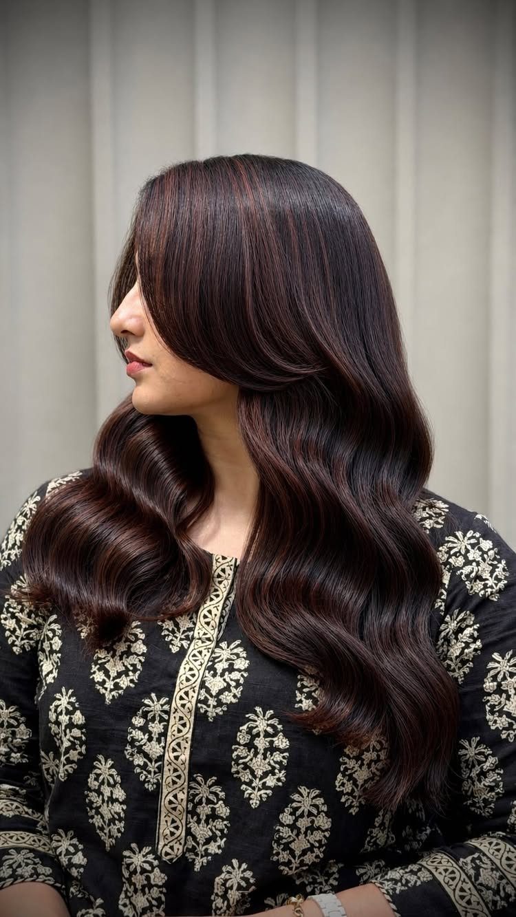 Woman with long wavy deep maroon hair wearing a black and gold outfit.