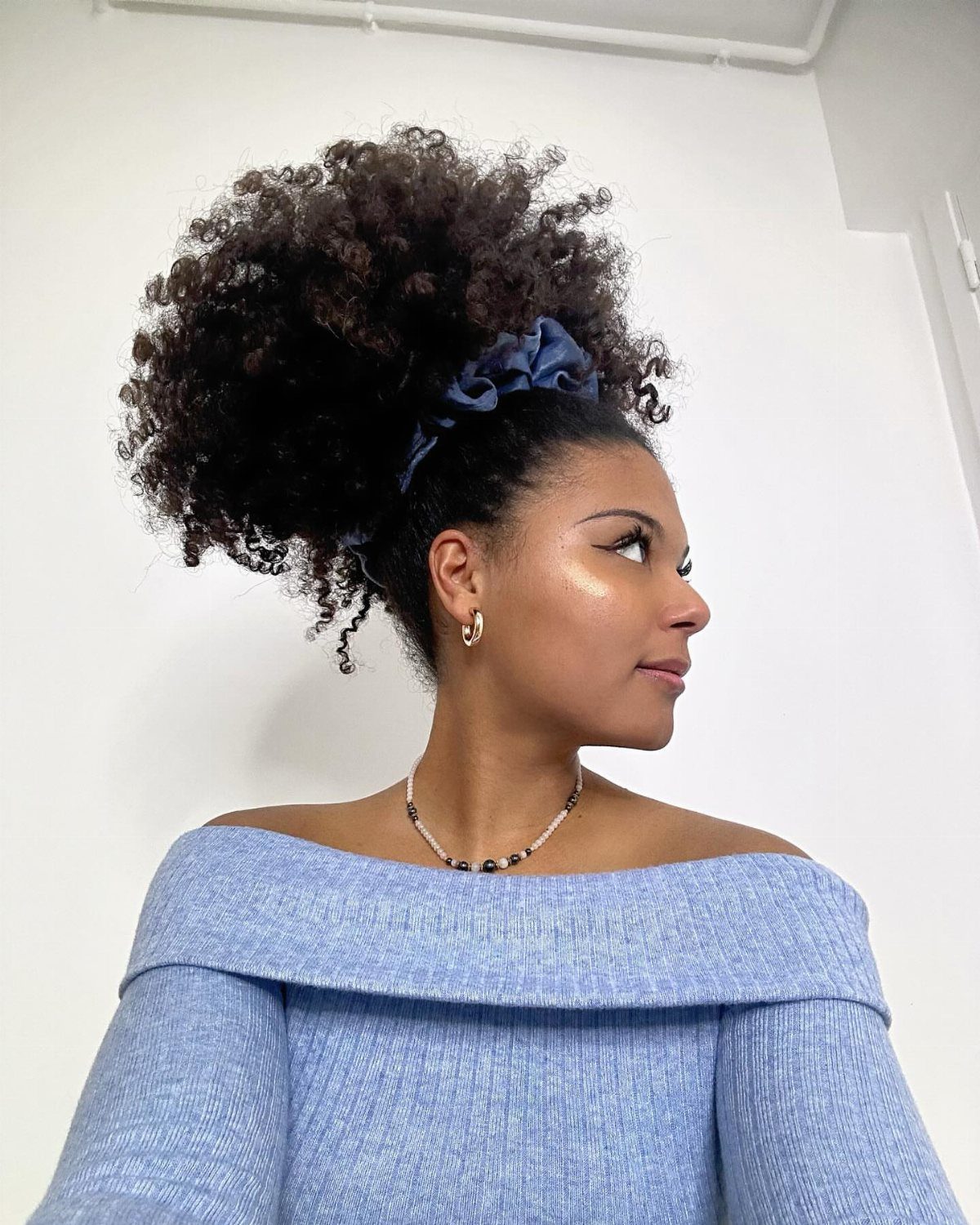 Woman with a high afro puff hairstyle secured by a blue scrunchie.
