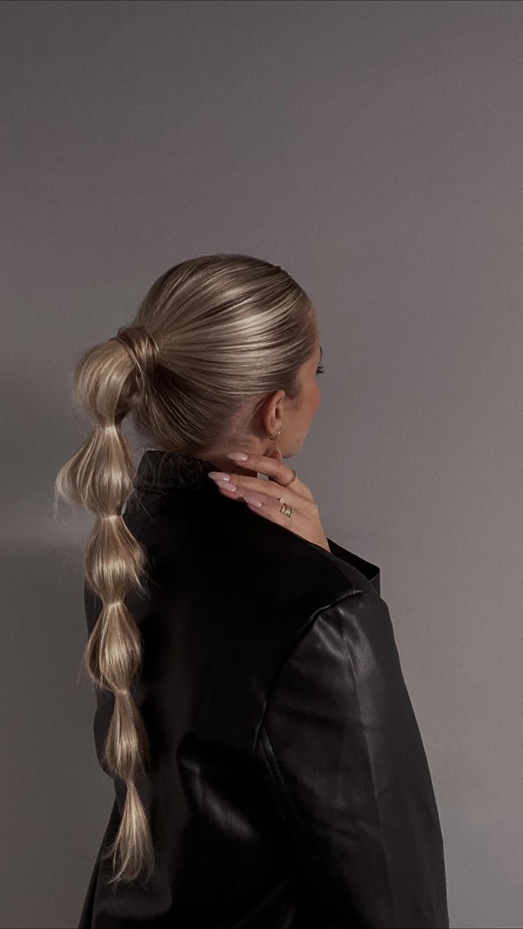 Blonde woman wearing a black leather jacket with a long bubble ponytail hairstyle.