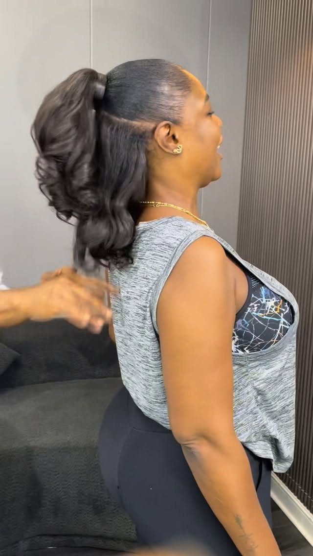 Woman with a high curly ponytail wearing a grey sleeveless top and black leggings.