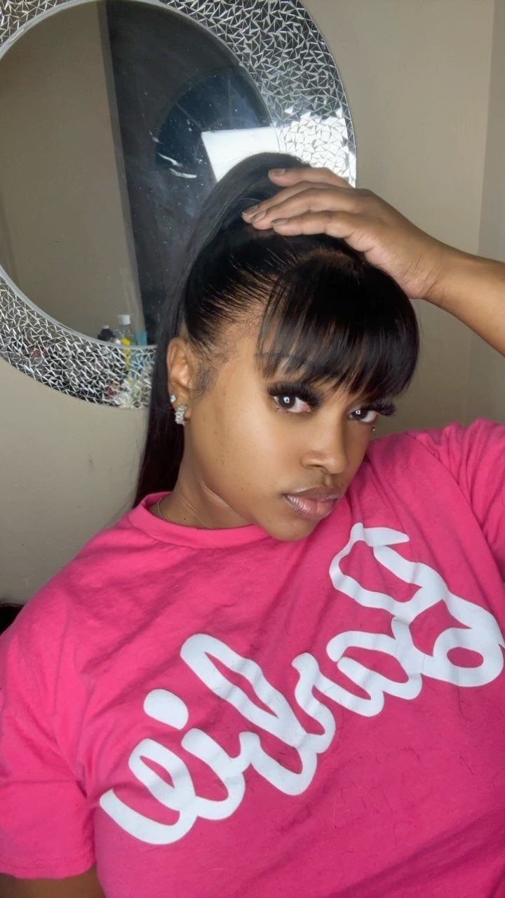 Woman with a high ponytail and straight bangs wearing a pink t-shirt.