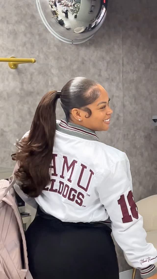 Woman with a sleek high ponytail wearing a white varsity jacket and black skirt.