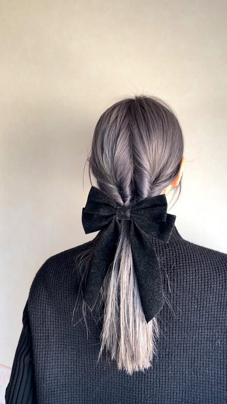 Silver-grey hair in a braided low ponytail tied with a black velvet bow.