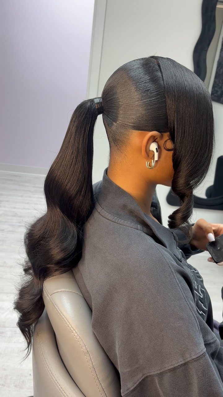 Woman with sleek dark hair styled in a wavy mid-height ponytail.
