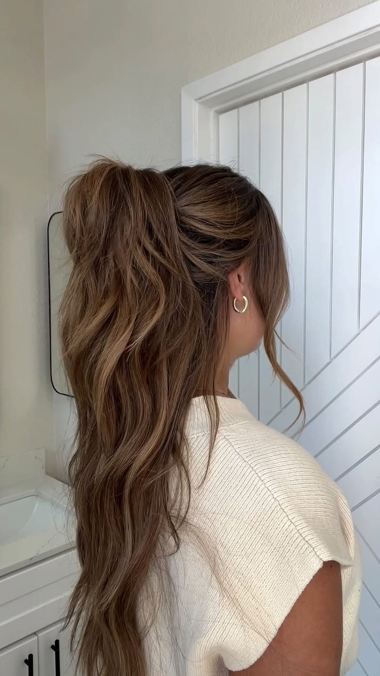 Woman with light brown hair in a high, voluminous textured ponytail and white top.
