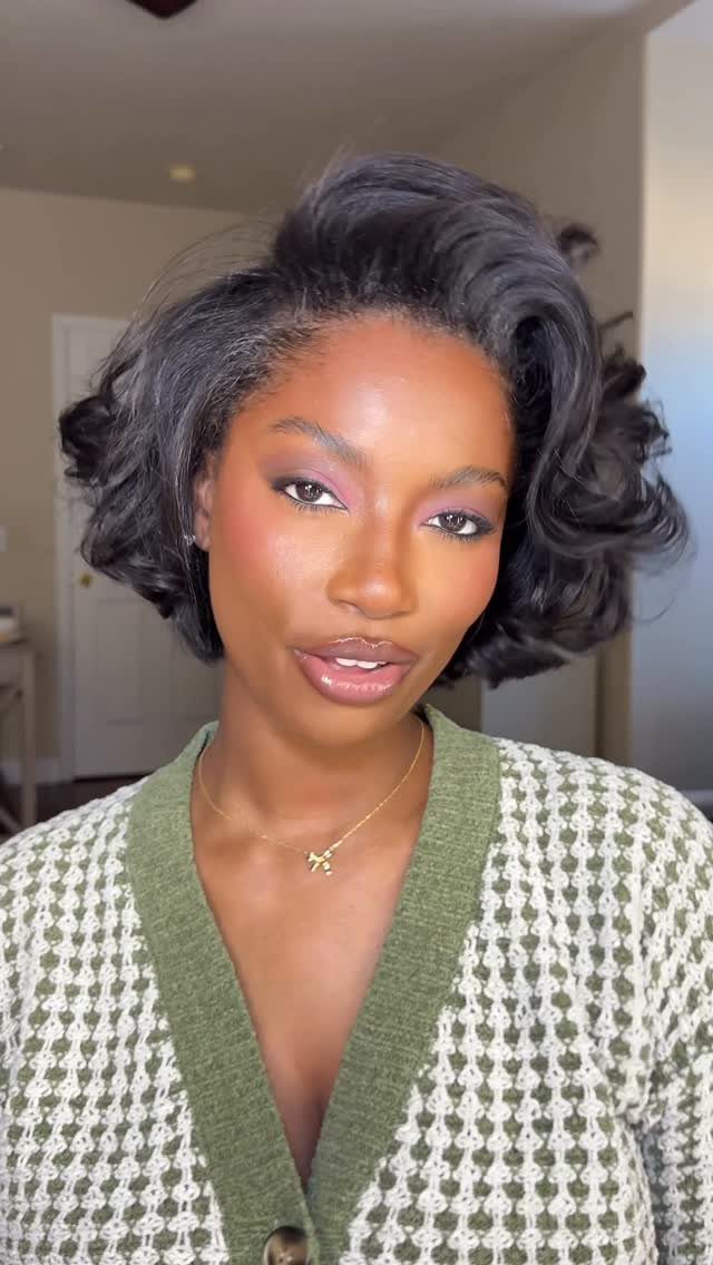 Woman with a voluminous dark curly bob haircut wearing a green textured cardigan.