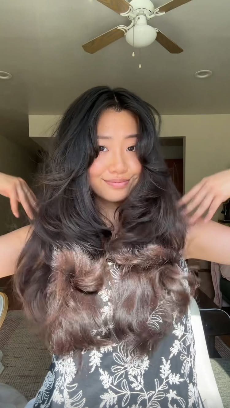 Woman with long dark layered curls and bangs posing in a floral dress.