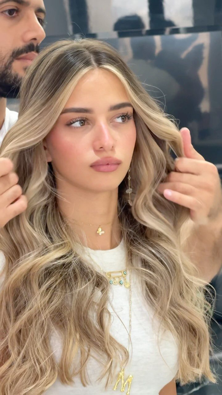 Woman with long blonde loose curly hair being styled by a hairdresser