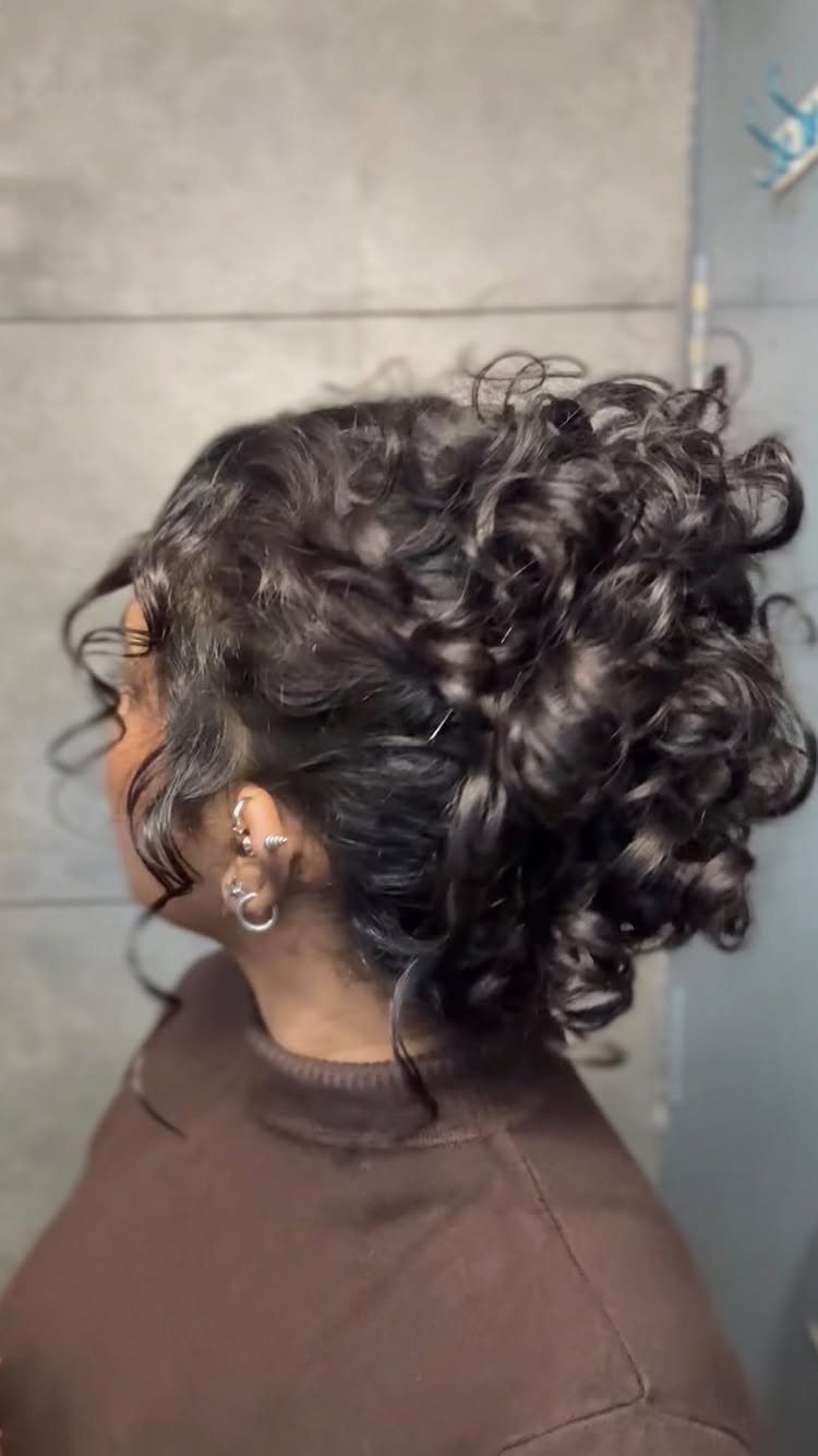 Dark curly hair styled into a voluminous messy bun from a side profile view