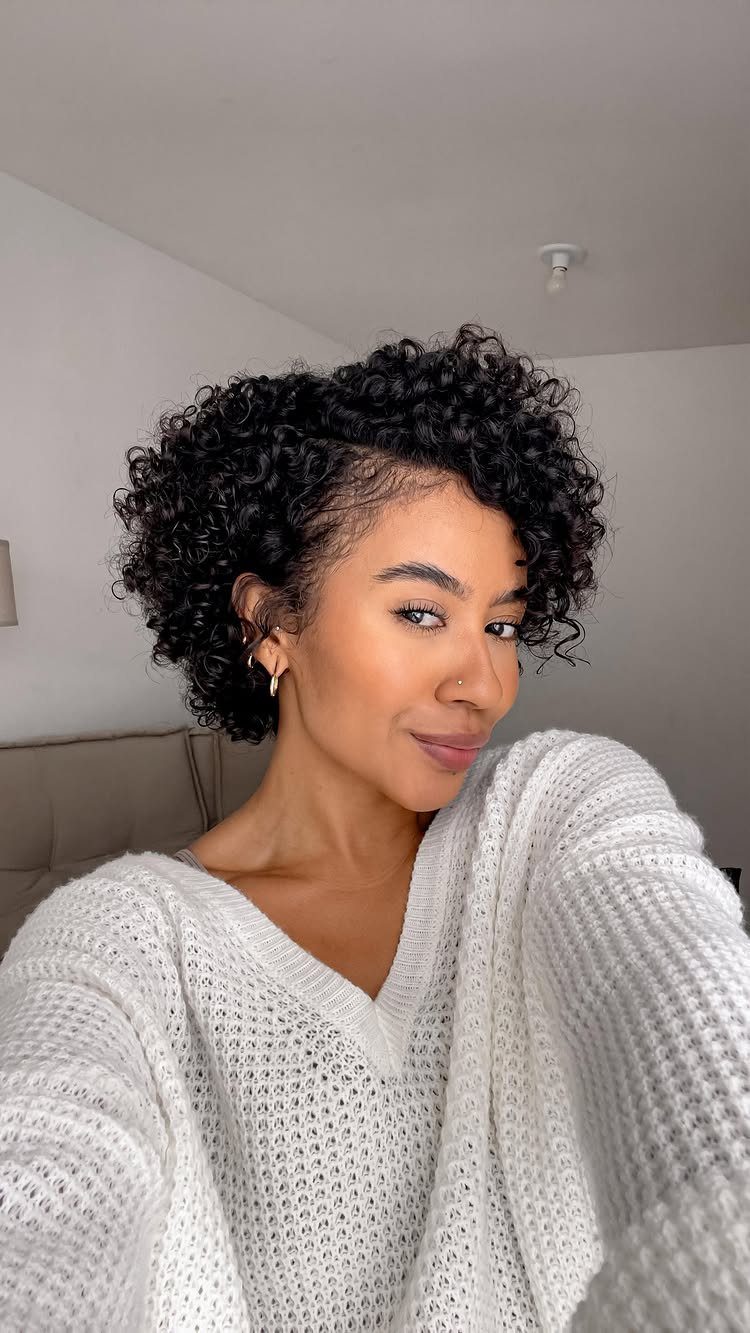 Woman with short black curly pixie cut wearing a white knit sweater.