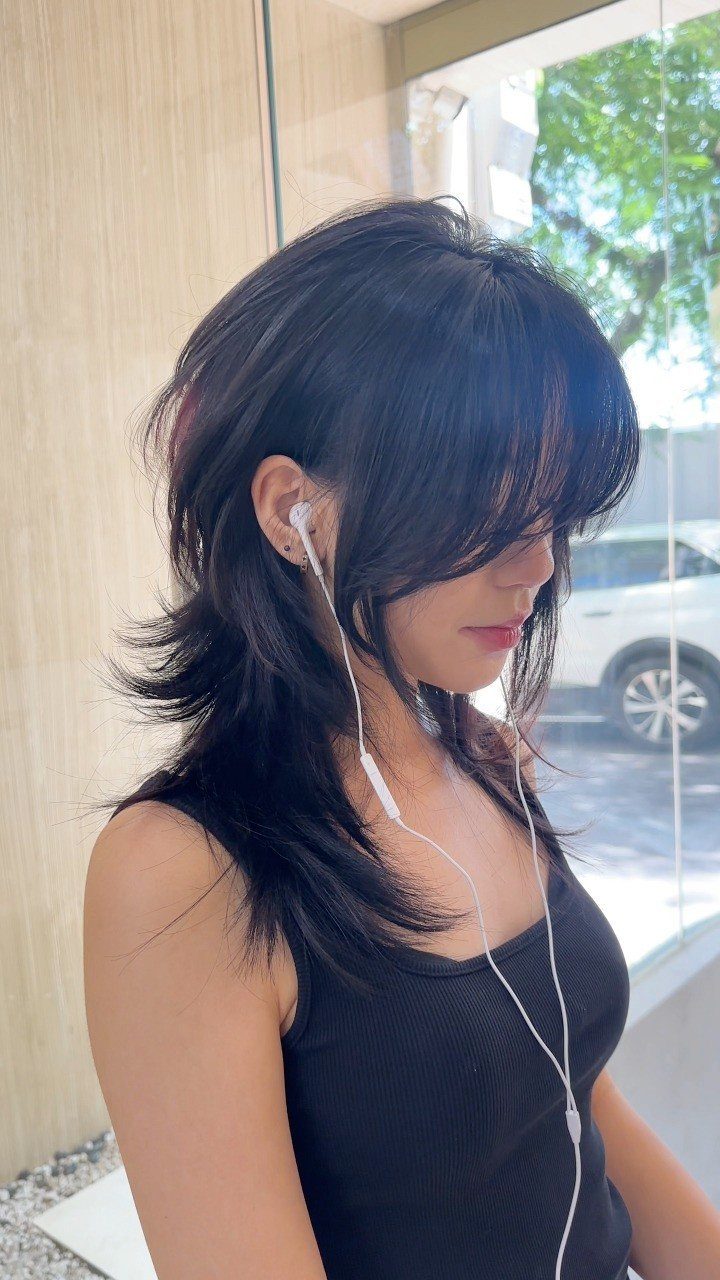 6 Hairstyles for Moms with Long Hair That Are Easy to Wear 2 Woman with a dark layered shag haircut and bangs wearing white wired earbuds.