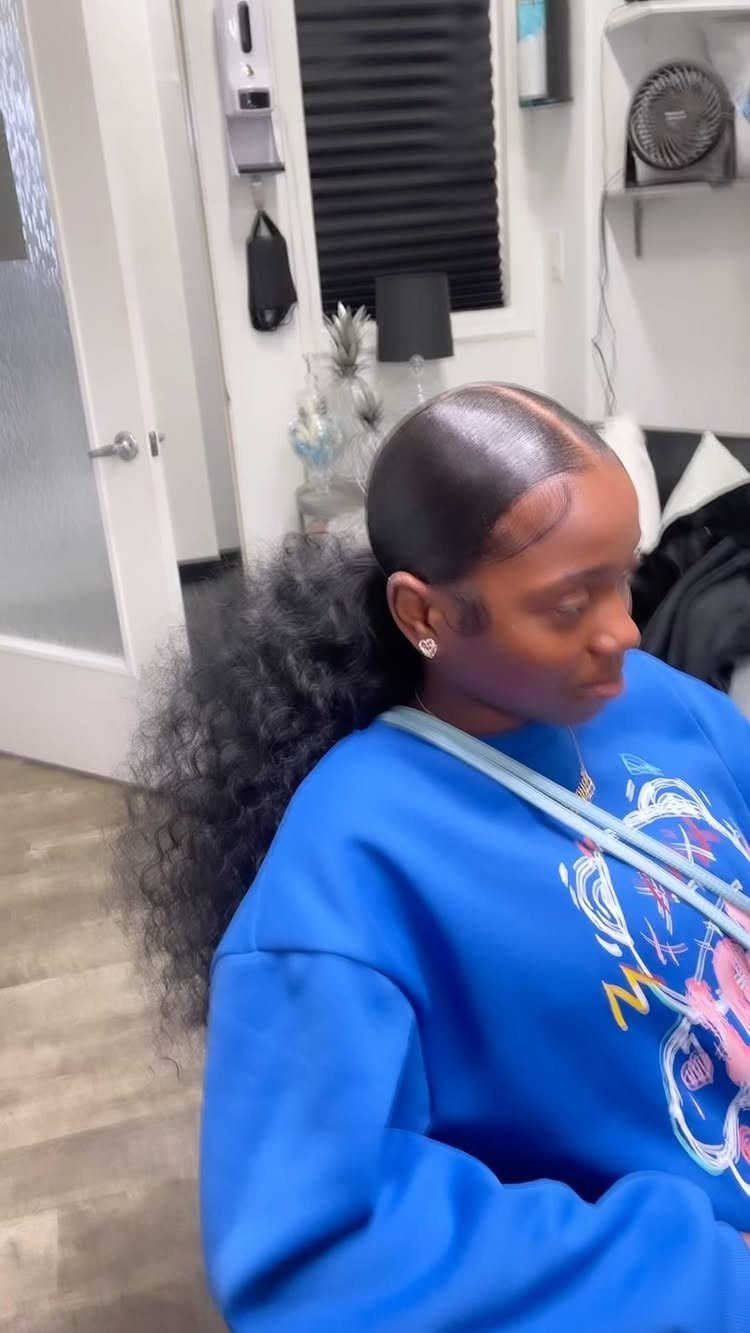 6 Hairstyles for Moms with Long Hair That Are Easy to Wear 6 Woman with a sleek low ponytail and voluminous curly hair wearing a blue sweatshirt.