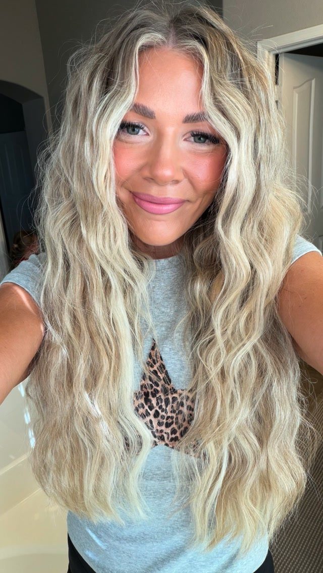 6 Hairstyles for Moms with Long Hair That Are Easy to Wear 3 Woman with long blonde textured waves and face-framing layers smiling for a selfie.