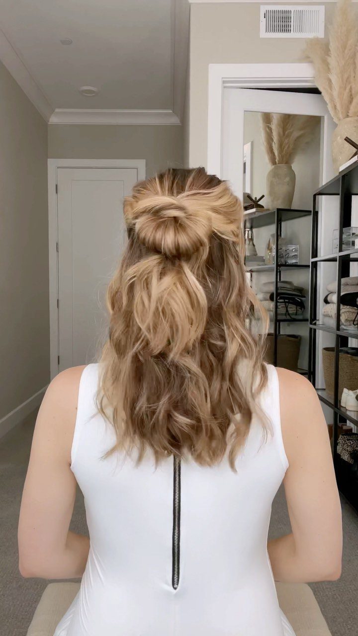 Blonde wavy hair styled in a small half-up bun and loose curls.