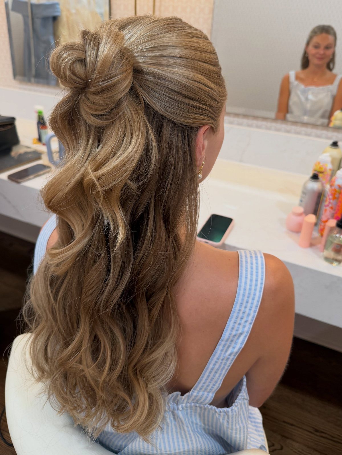 Blonde hair styled in a half-up bun with loose waves flowing down.