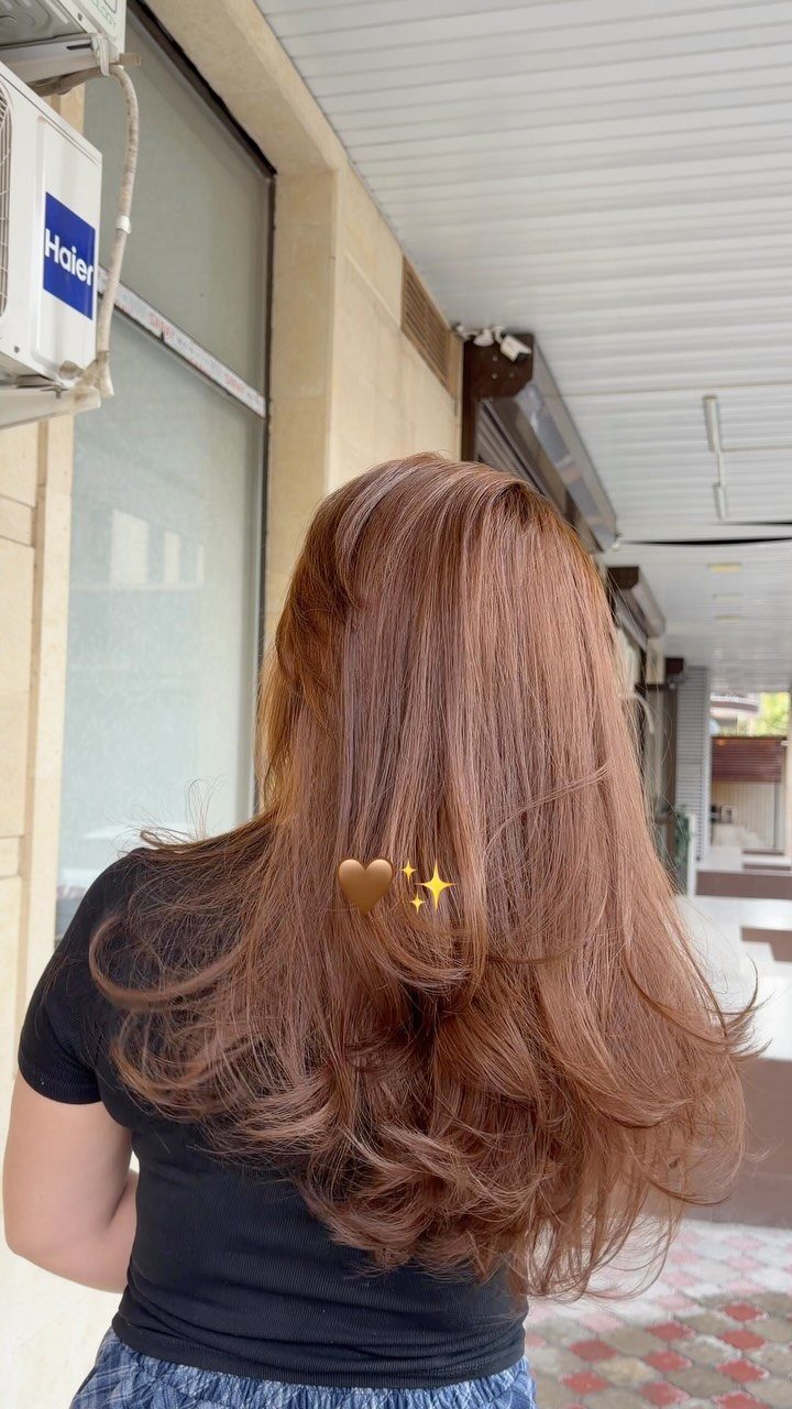 Woman with long wavy hazelnut hair featuring warm auburn hues from behind.