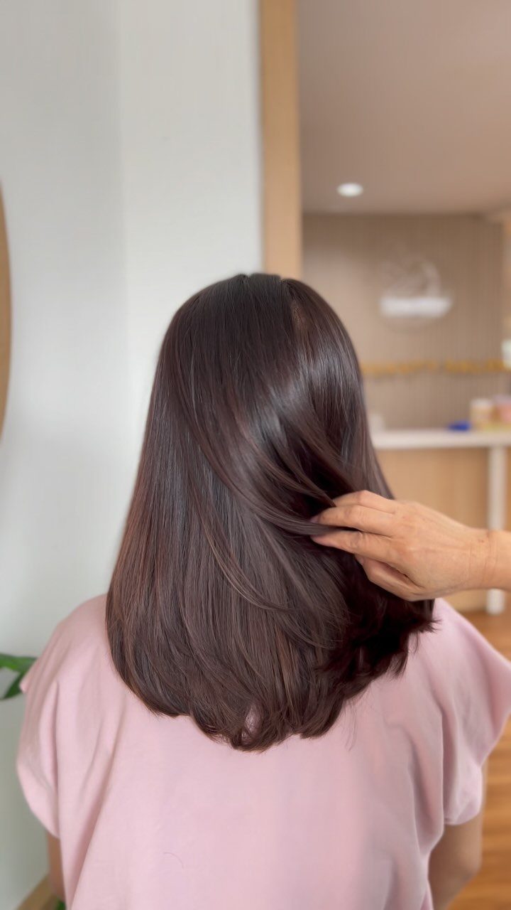 Woman with smooth hazelnut brown hair seen from behind in a bright room