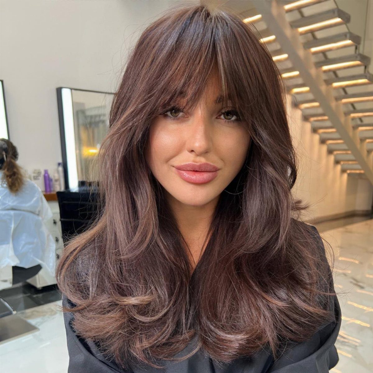 Woman with long wavy hazelnut brown hair and bangs in a hair salon