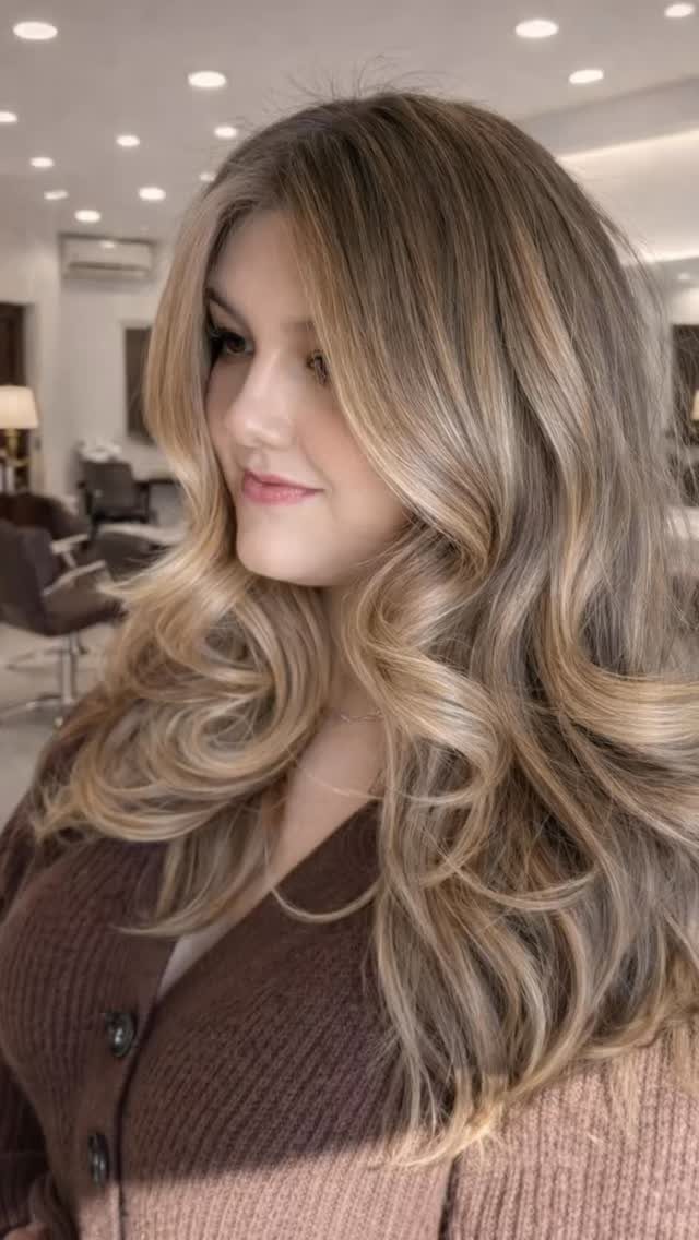 8 Honey Blond with Highlights Ideas for Every Look 5 Woman with long wavy honey blonde balayage hair wearing a brown cardigan.