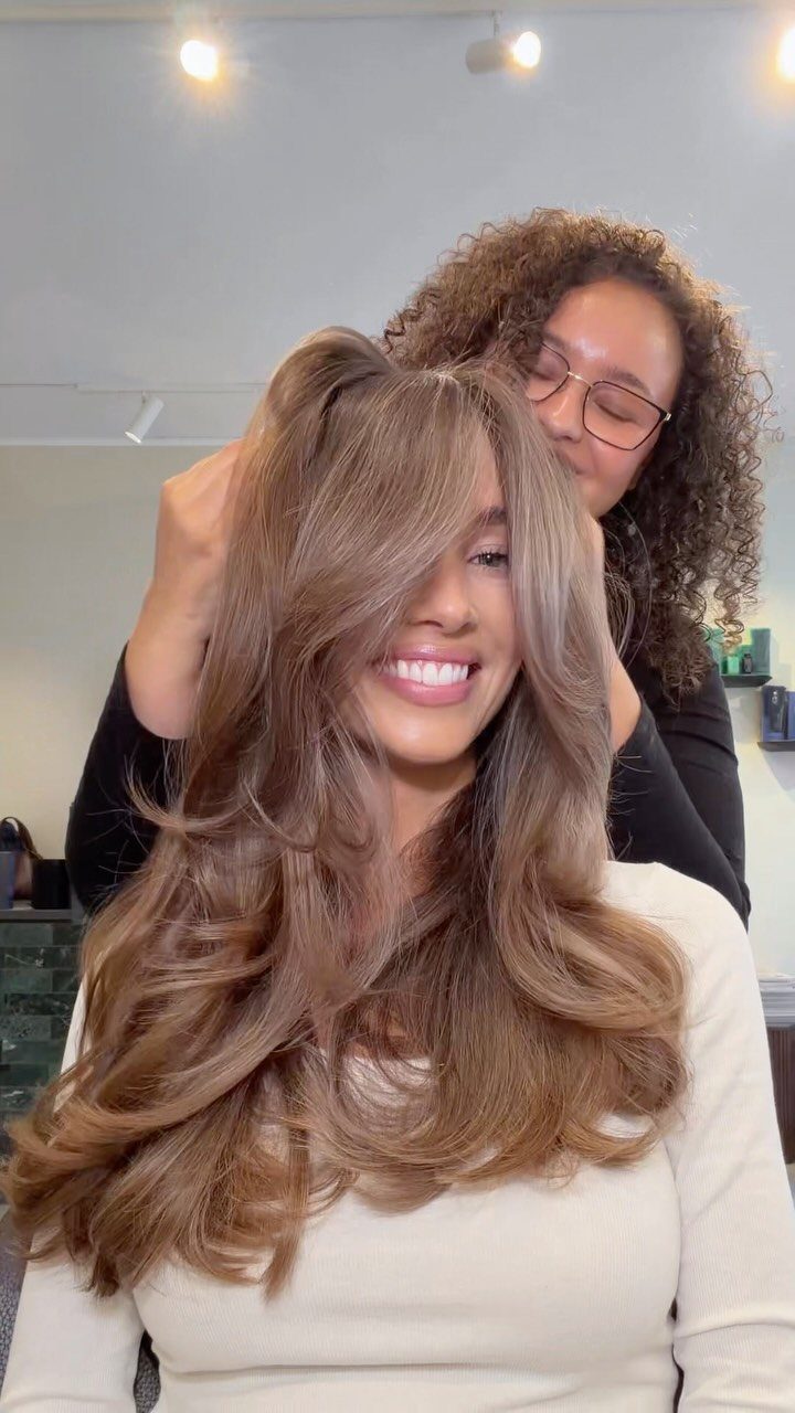 8 Honey Blond with Highlights Ideas for Every Look 8 Woman with honey dipped brunette hair smiling while a stylist adjusts her waves.