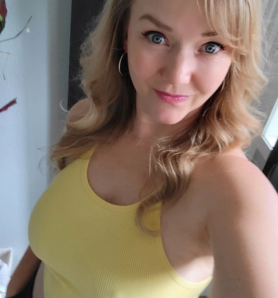 8 Honey Blond with Highlights Ideas for Every Look 4 Woman with wavy honey blonde hair wearing a yellow ribbed tank top.