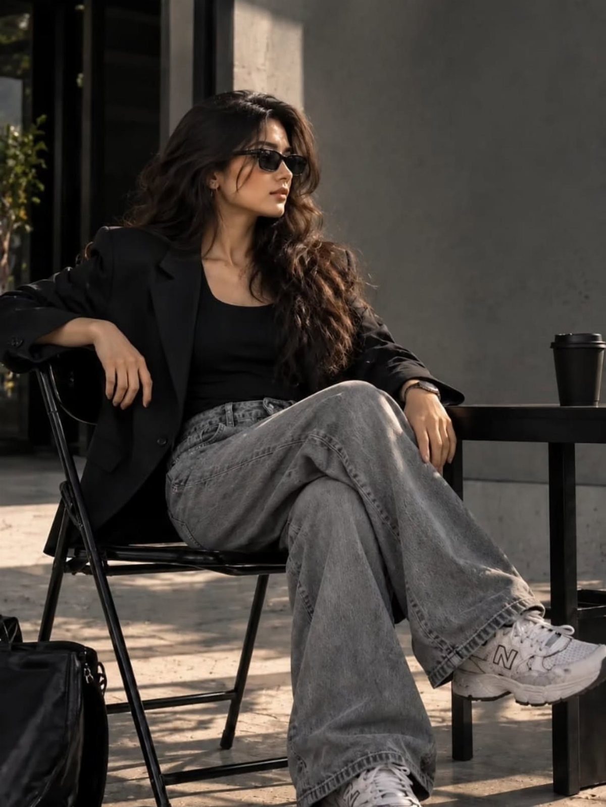 Woman wearing a black blazer and wide-leg blue jeans sitting outdoors on a chair.
