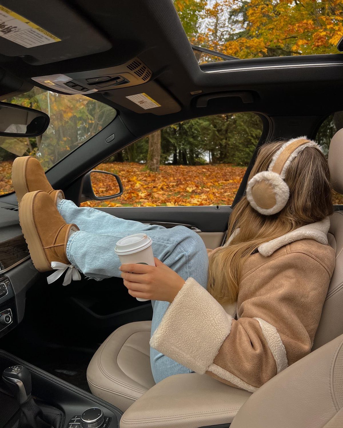 Woman in a car wearing tan boots, blue jeans, and a shearling jacket.