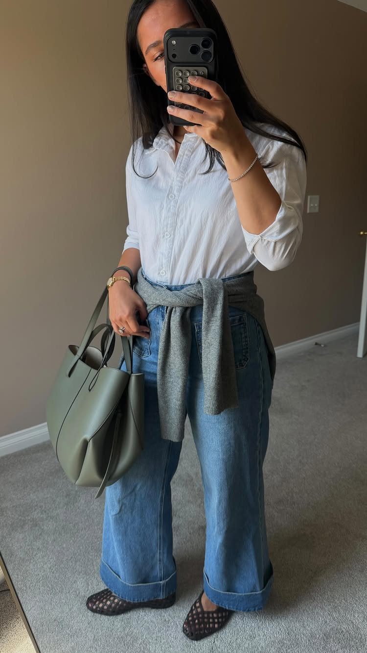 Woman wearing a white button-down blouse, blue wide-leg jeans, and olive green handbag.