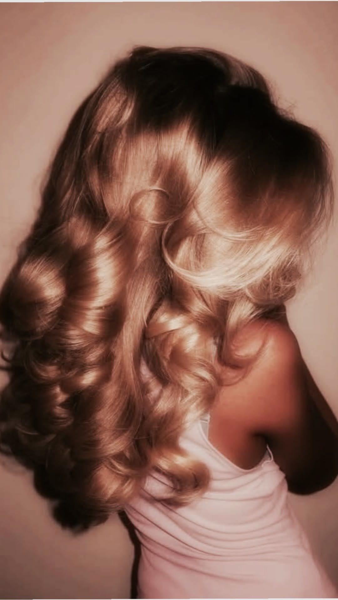 Woman with voluminous honey-blonde curls flowing over her shoulder in a glamorous style.