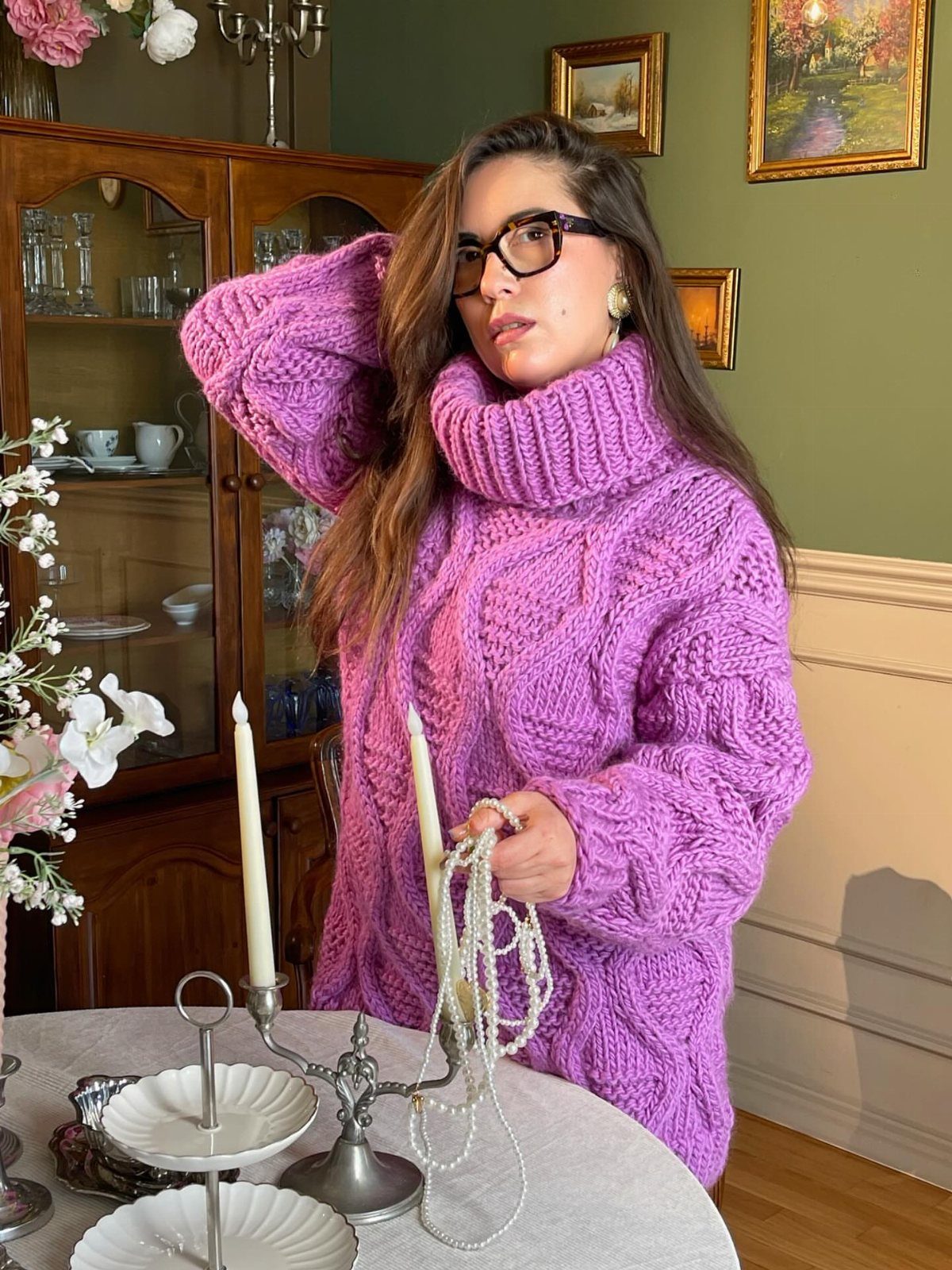 Woman wearing an oversized amethyst purple cable-knit turtleneck sweater in a classic room.