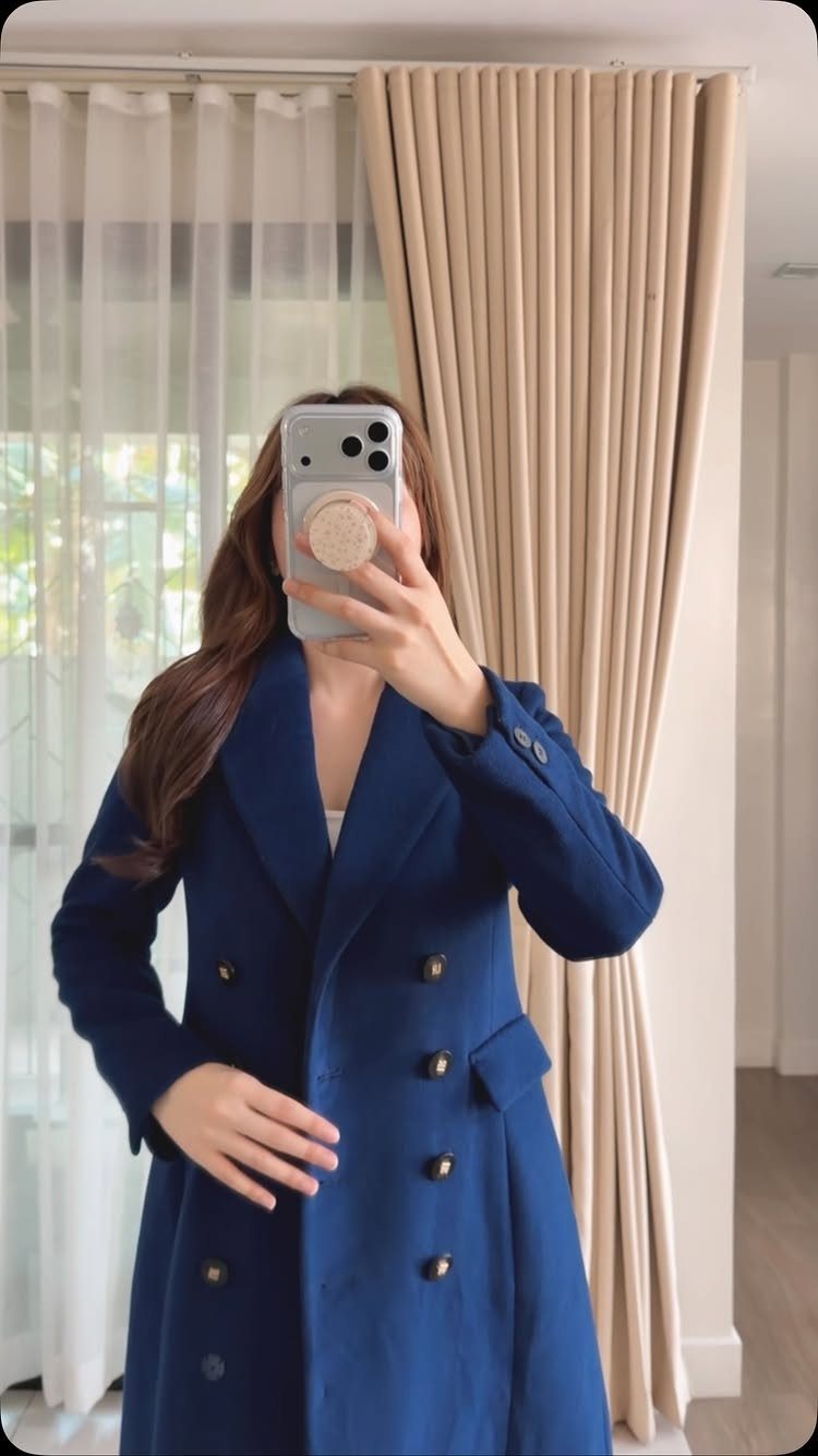 Woman wearing a long cobalt blue wool coat posing for a mirror selfie.
