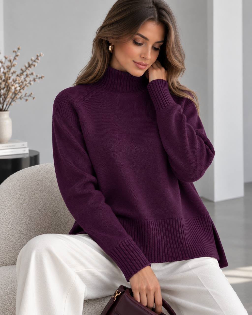 Woman wearing a deep purple sweater and white wide-leg trousers sitting on a chair.