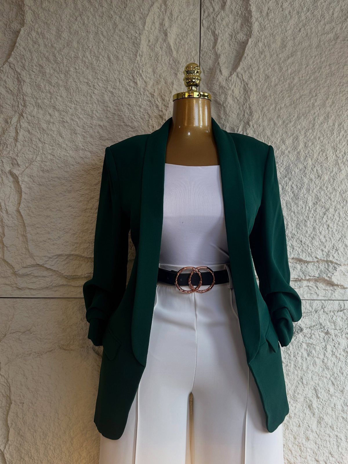 Emerald green blazer and white trousers on a mannequin against a stone wall.