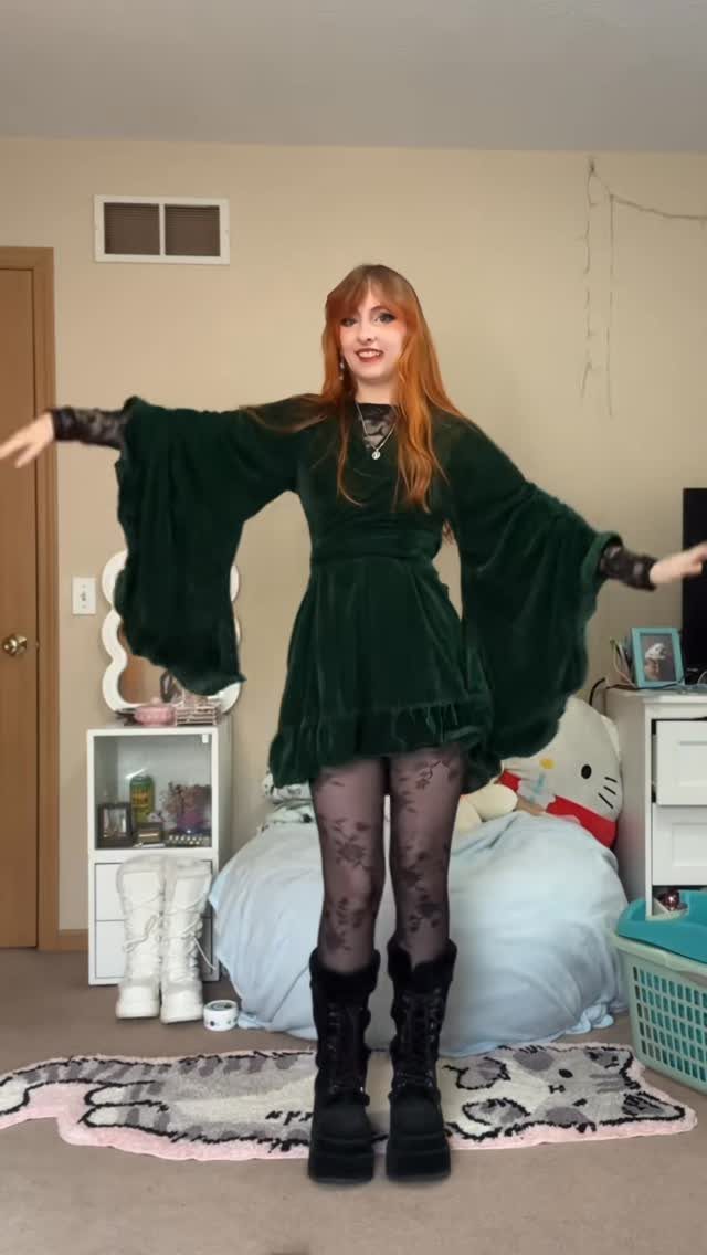 Woman wearing an emerald green velvet wrap dress with black patterned tights and boots.