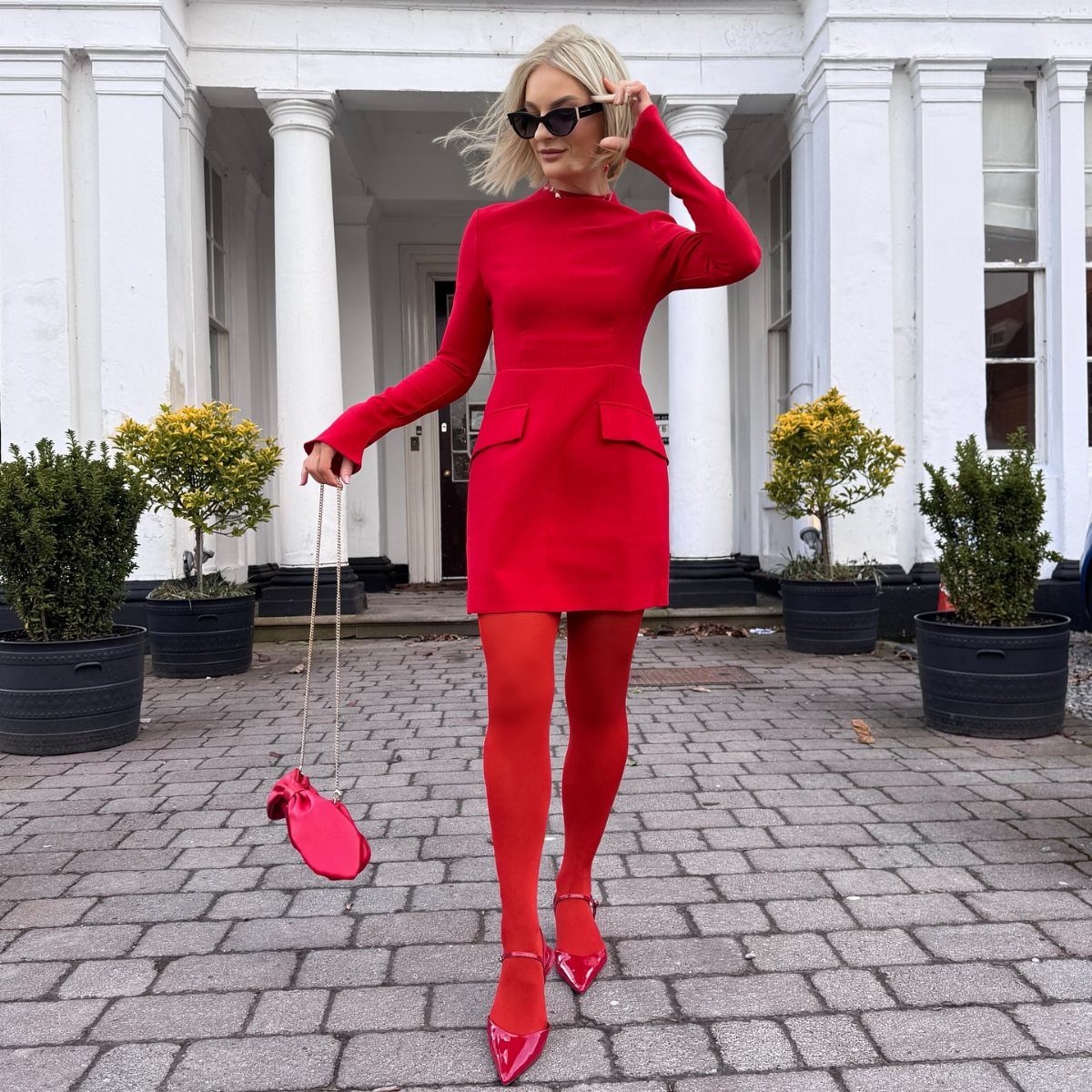 Woman in a monochromatic bright red dress, tights, and heels posing outdoors.