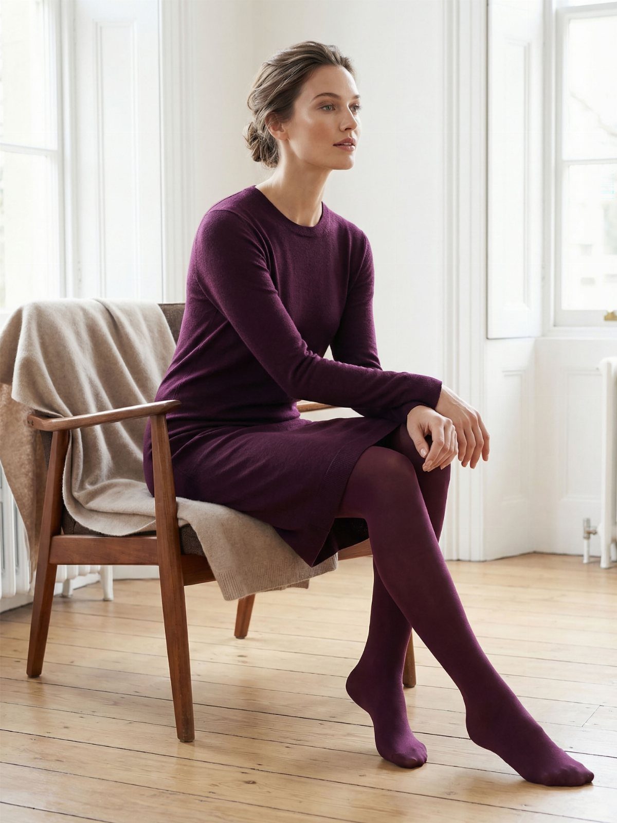 Woman wearing a plum-colored dress and matching tights sitting in a wooden chair.