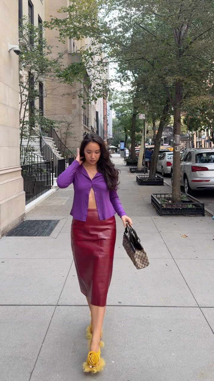 Woman in purple shirt and burgundy leather skirt walking on a city sidewalk